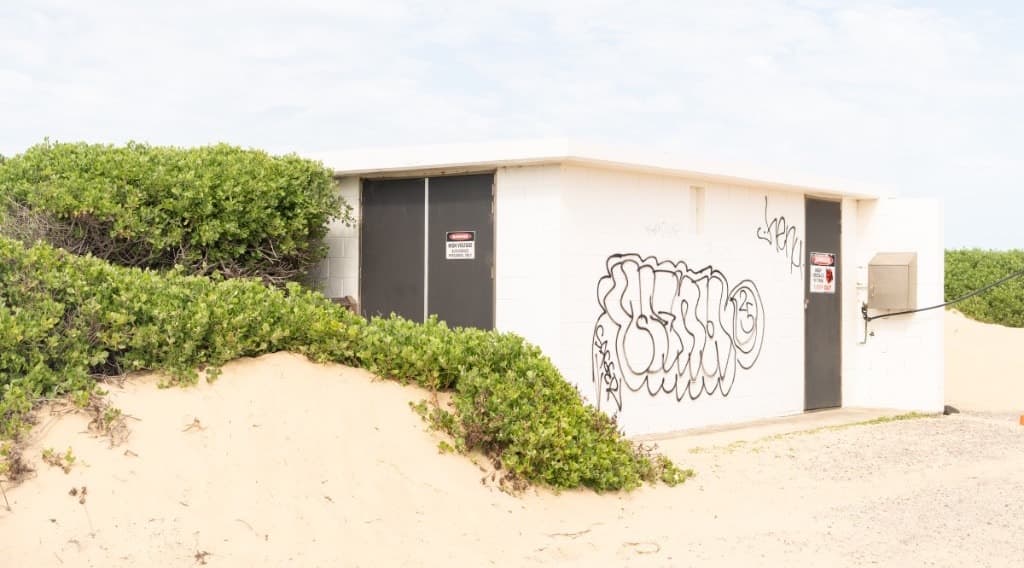 A white concrete hut with graffiti, half buried in a grassy sand dune