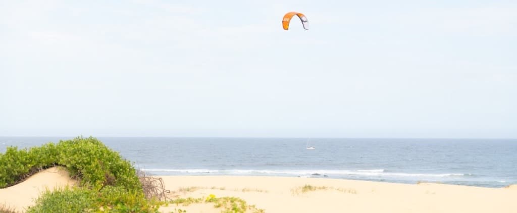 An orange kite high above a quiet beach and dune grass